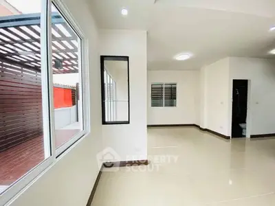 Spacious modern living room with large windows and sleek tile flooring, adjacent to a stylish outdoor patio.