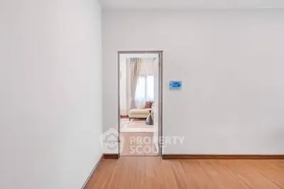 Spacious interior with wooden flooring and a glimpse of a cozy living room through the doorway.