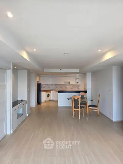 Spacious open-plan living room with modern kitchen and dining area, featuring sleek wooden flooring and ample natural light.