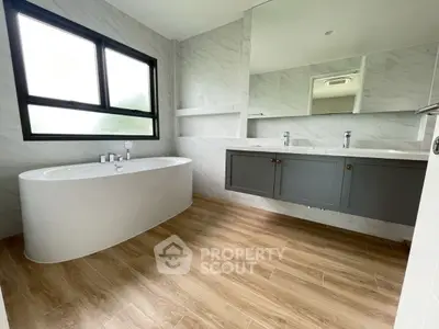 Spacious modern bathroom with elegant bathtub and large mirror, featuring sleek wooden flooring.