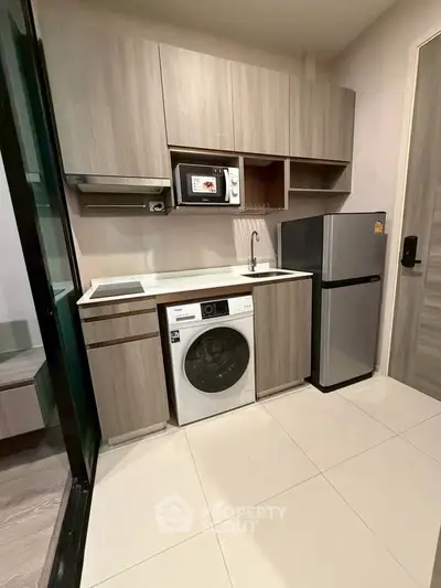 Modern kitchen with washing machine, fridge, and microwave in compact layout.