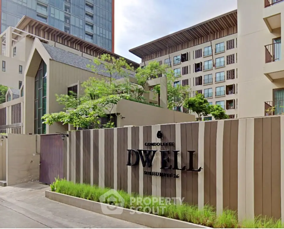 Modern condominium entrance with stylish architecture and lush greenery in vibrant urban setting.