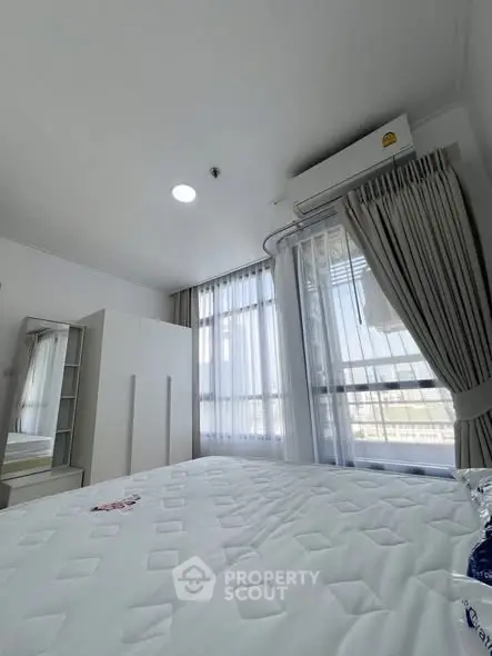 Bright bedroom with large windows and modern furnishings, featuring an air conditioning unit.