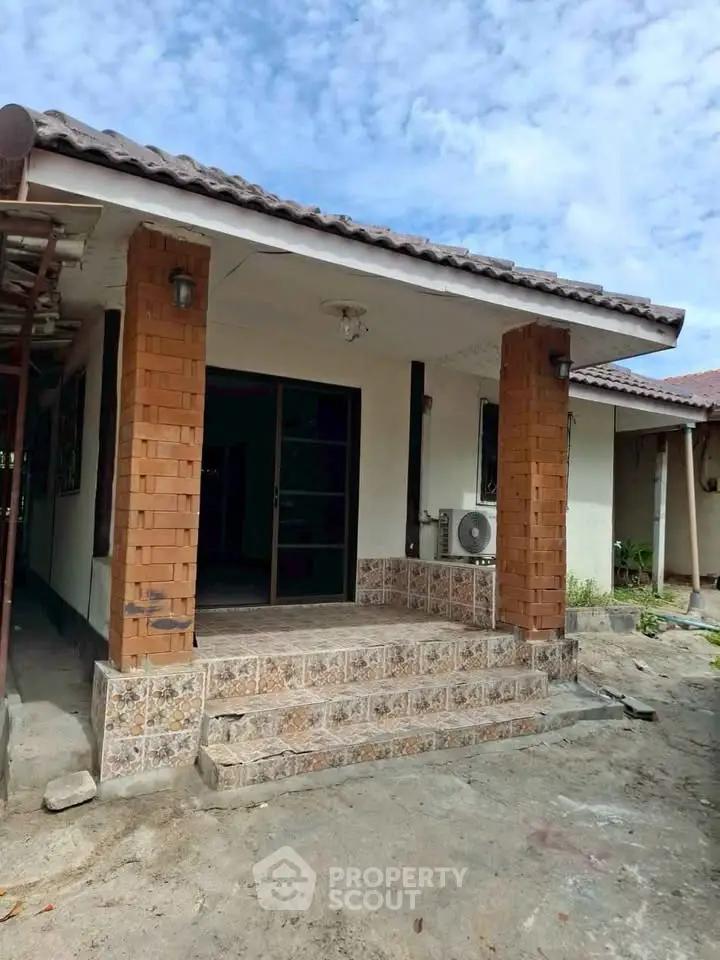 Charming single-story home with tiled steps and brick columns under a clear blue sky.