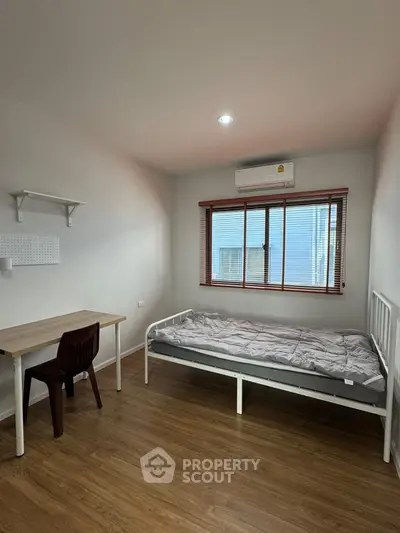Minimalist bedroom with wooden flooring, single bed, desk, and window view.