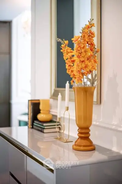 Elegant interior decor with orange flowers and candles on a sleek white console table.