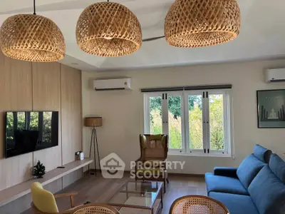 Charming living room with modern decor and large windows offering lush garden views.