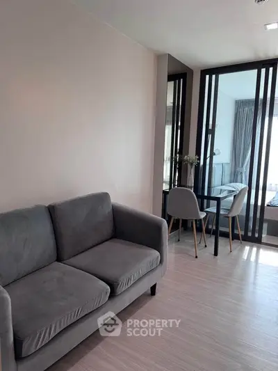 Modern living room with sleek gray sofa and dining area in open-plan apartment