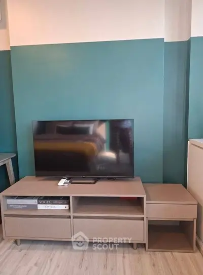Modern living room with stylish TV stand and flat-screen TV, featuring teal accent wall and sleek flooring.