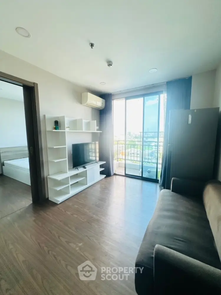 Modern living room with balcony and city view, featuring sleek furniture and natural light.
