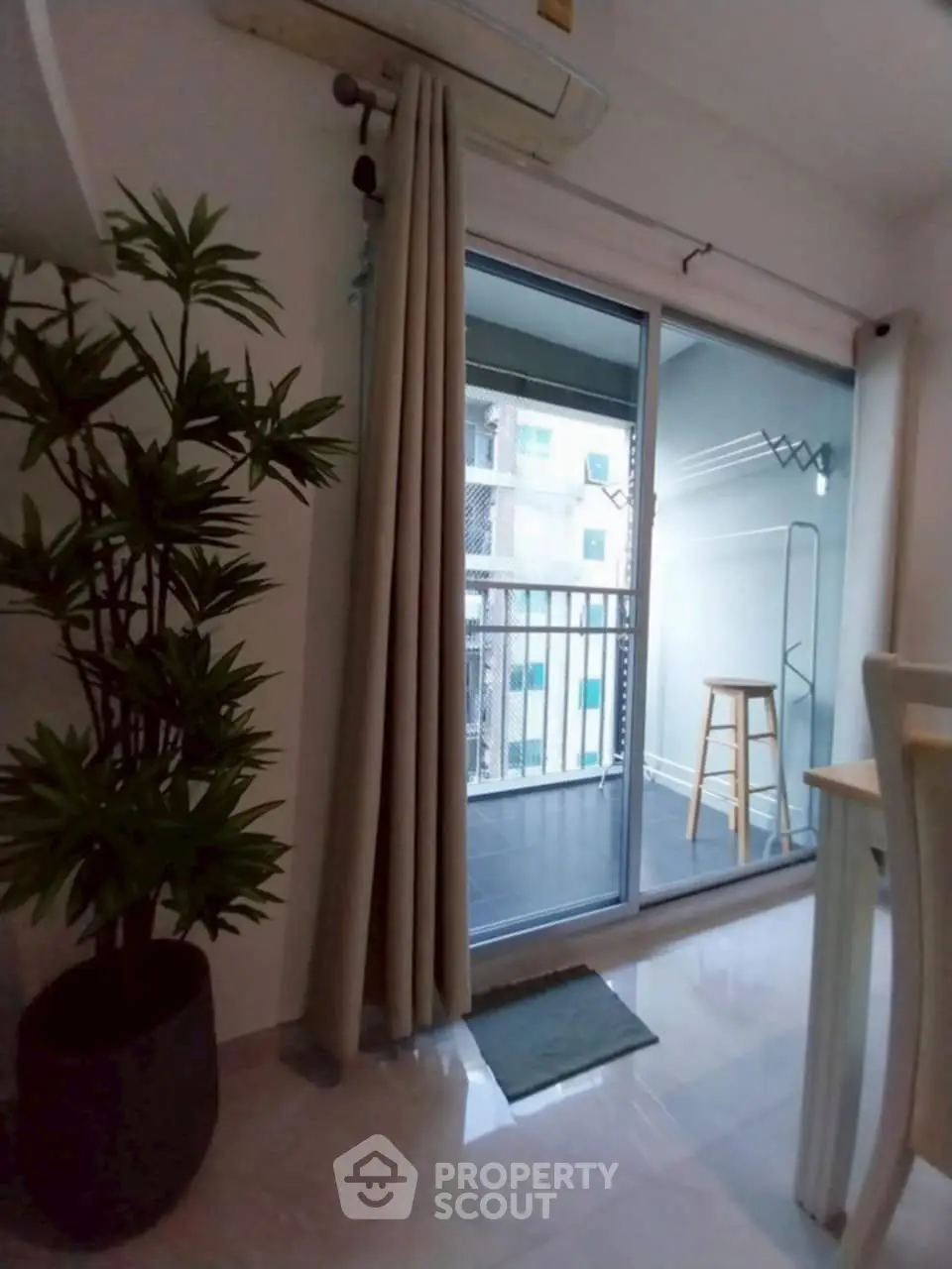 Modern apartment with sliding glass door leading to a cozy balcony, featuring a potted plant and dining area.