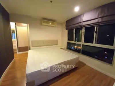Spacious bedroom with large windows and wooden flooring in modern apartment.