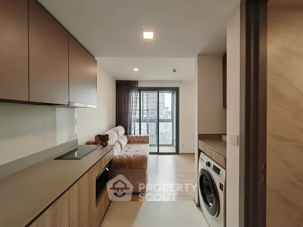 Modern apartment interior with sleek kitchen and cozy living room, featuring a washing machine and city view.