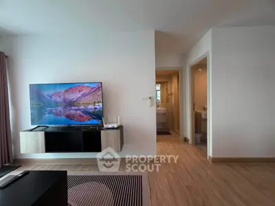 Modern living room with sleek TV setup and wooden flooring, adjacent to a compact bathroom.
