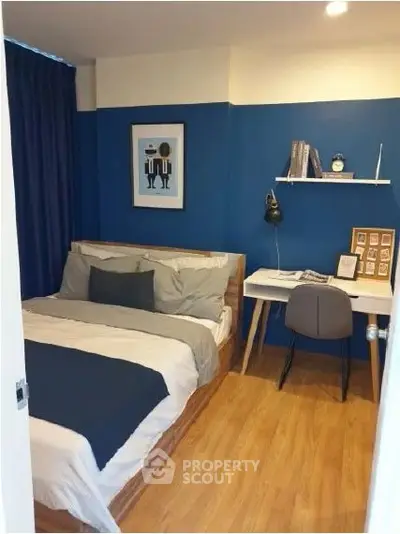 Cozy bedroom with modern decor and study area, featuring blue accent wall and wooden flooring.