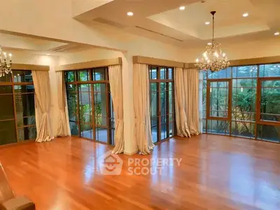 Spacious living room with elegant chandeliers and large windows offering garden views.