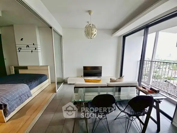 Modern open-plan living room with glass doors leading to a balcony and a cozy bedroom area.