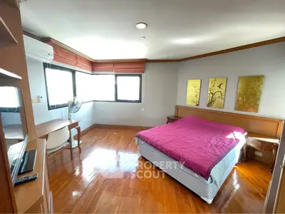 Spacious bedroom with wooden flooring and large windows offering natural light.