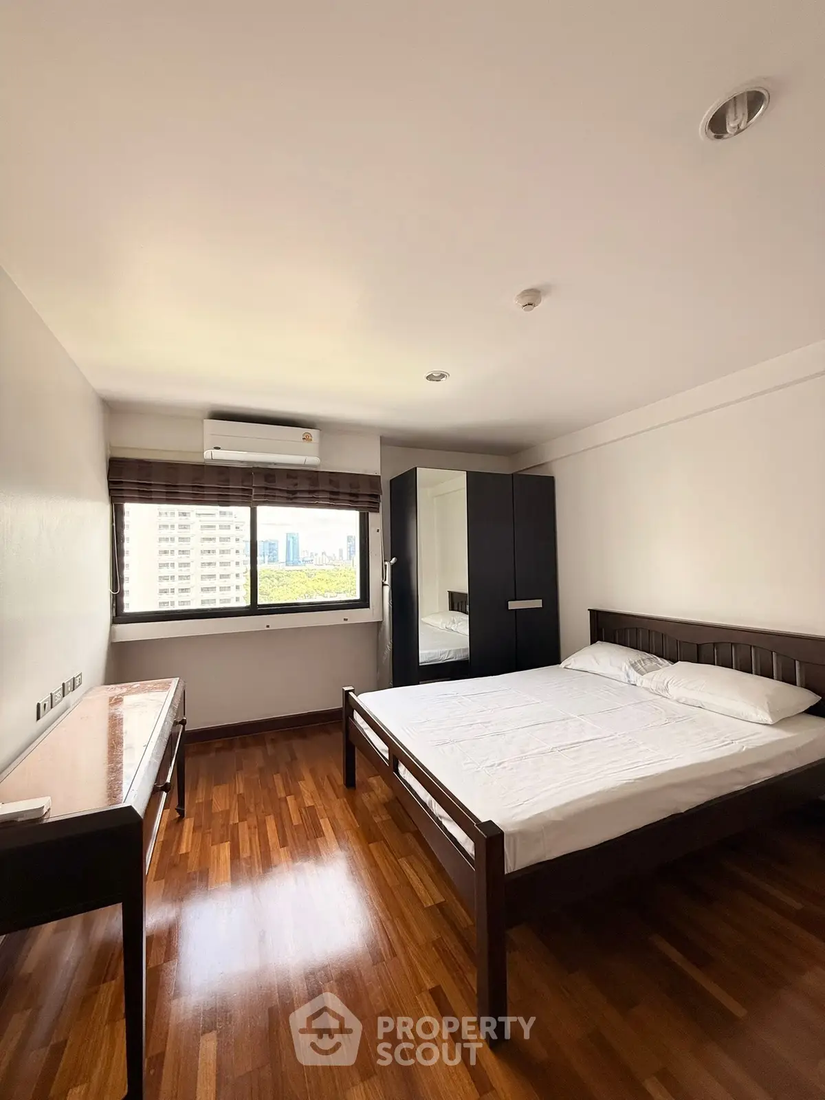 Spacious bedroom with wooden flooring and city view in modern apartment