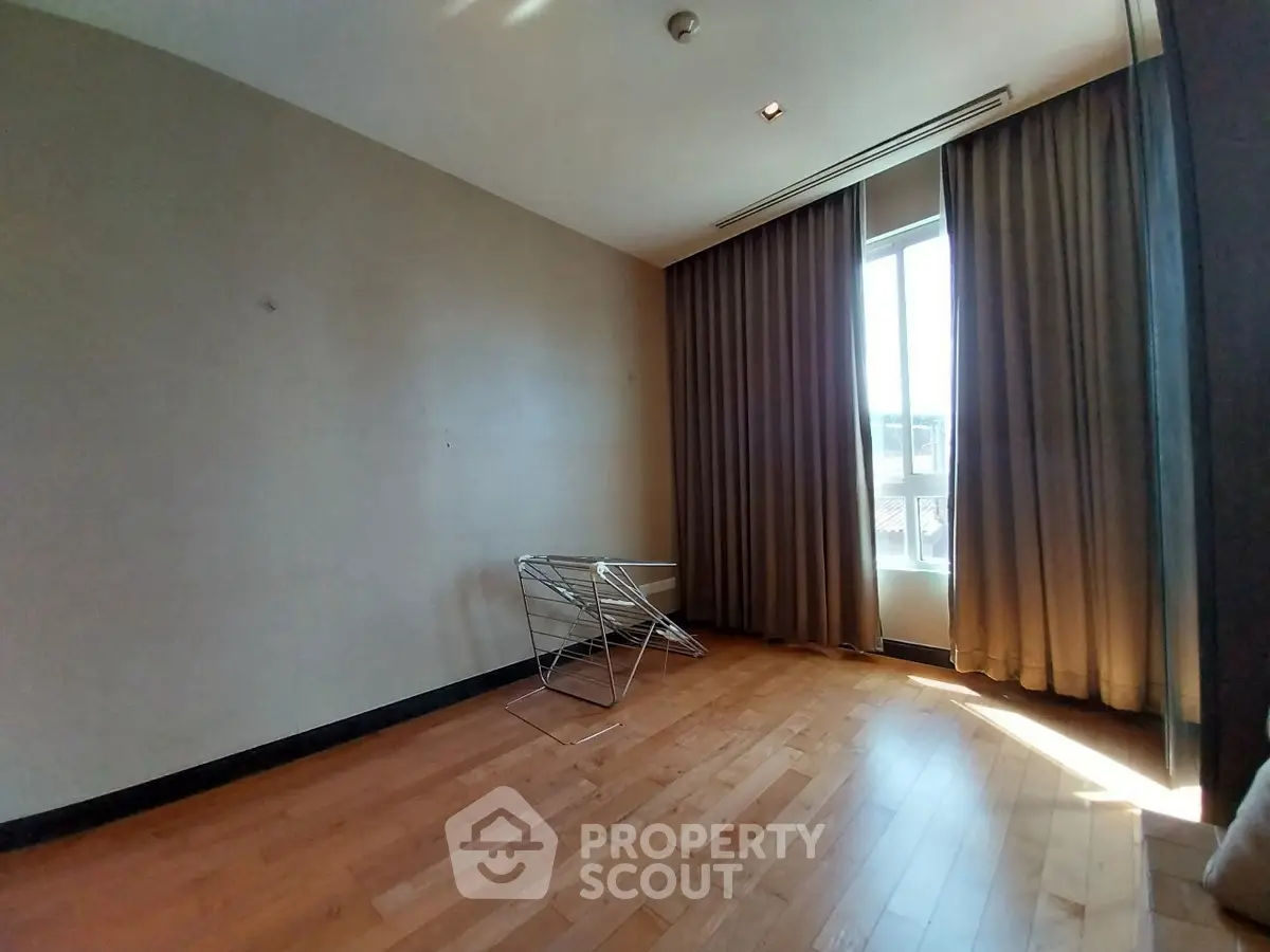 Spacious empty room with wooden flooring and large window with curtains