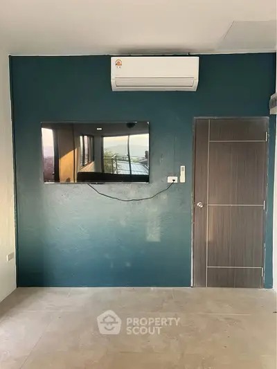 Modern room with teal accent wall, mounted TV, and air conditioning unit.