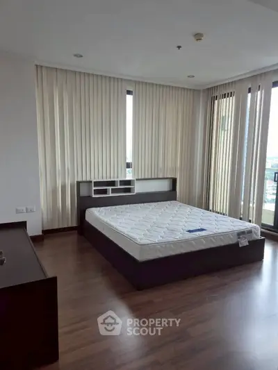 Spacious bedroom with large windows and modern design in a high-rise apartment.