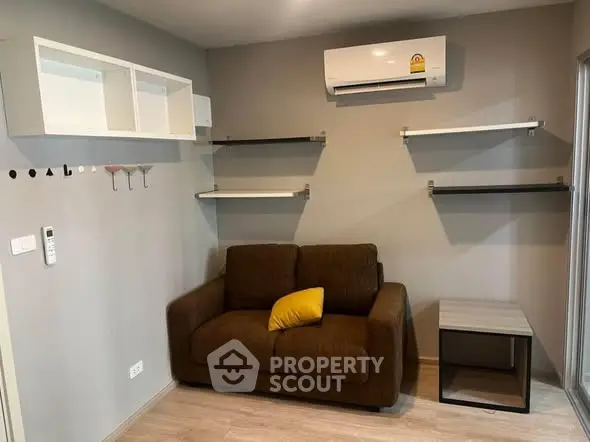Cozy living room with brown sofa, wall-mounted shelves, and air conditioning unit.