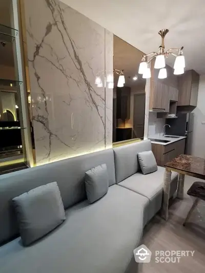 Elegant compact living space with modern grey sofa, marble wall feature, and chic kitchenette with high-end appliances, perfect for urban living.