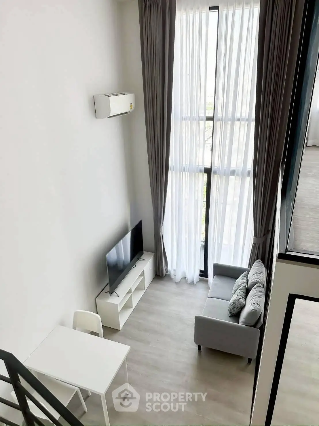 Modern loft-style living room with high ceilings and large windows, featuring a cozy sofa and sleek TV setup.