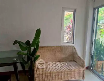 Charming living room with wicker sofa and lush garden view through glass doors.