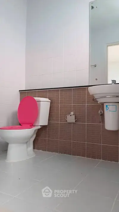 Modern bathroom with pink toilet seat and sleek white tiles.