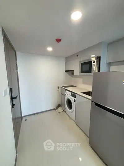 Modern compact kitchen with washing machine and microwave in sleek apartment.