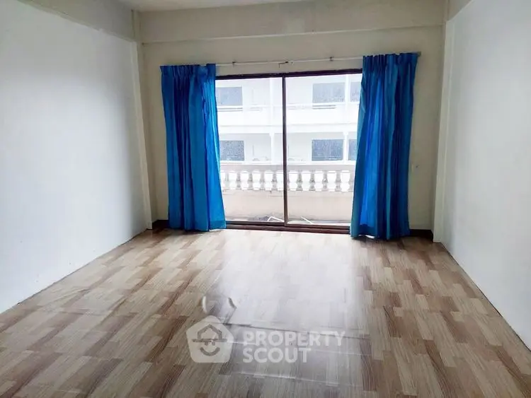 Spacious empty room with large window and blue curtains, ideal for customization.