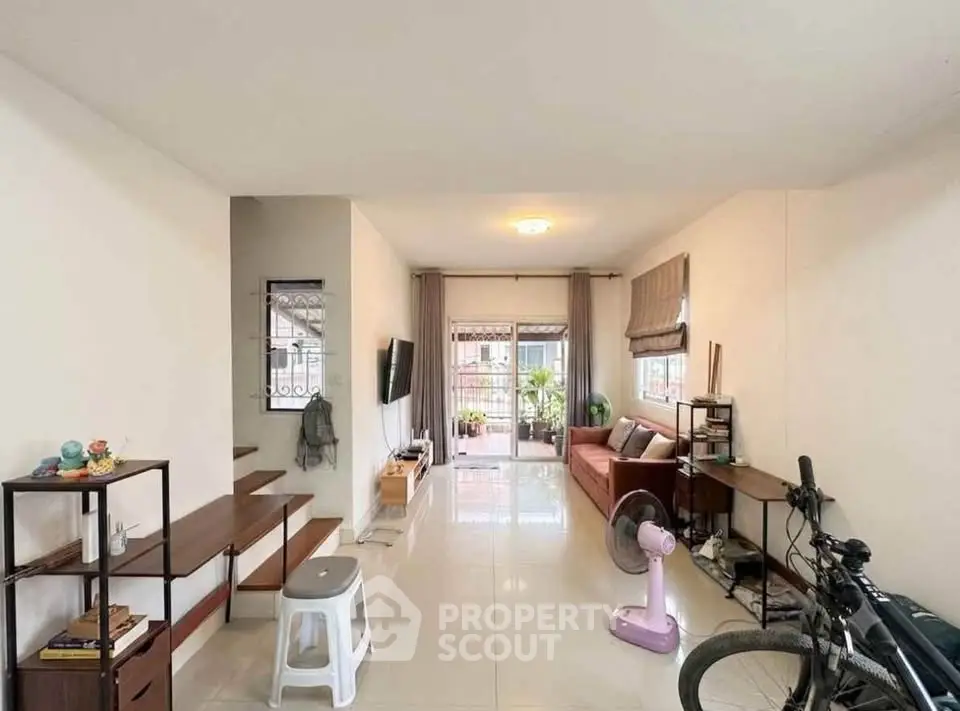 Spacious living room with modern decor and natural light, featuring a cozy seating area and stylish shelving.