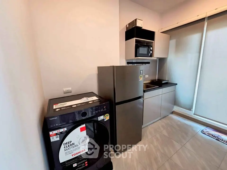 Modern kitchen with sleek appliances including fridge, microwave, and washing machine in a compact layout.