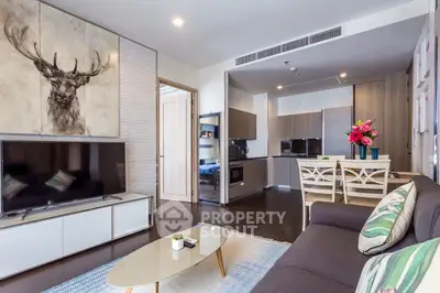 Modern living room with stylish decor and open kitchen layout, featuring a large TV and contemporary furniture.
