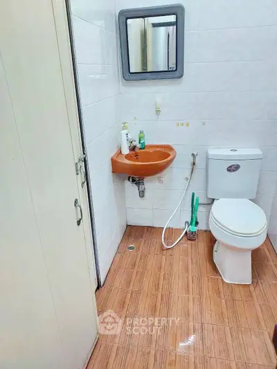 Compact bathroom with orange sink and white toilet, featuring tiled walls and floor.