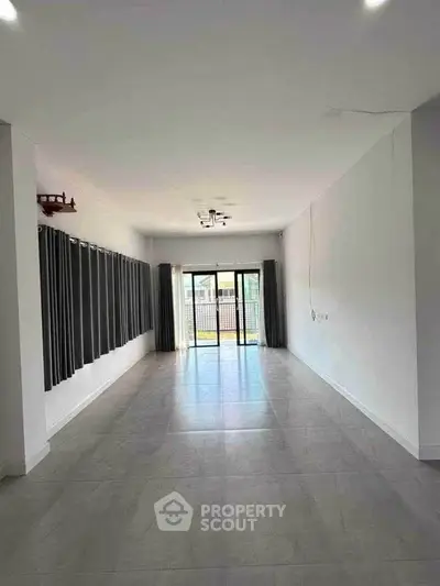 Spacious empty living room with large windows and modern tile flooring.