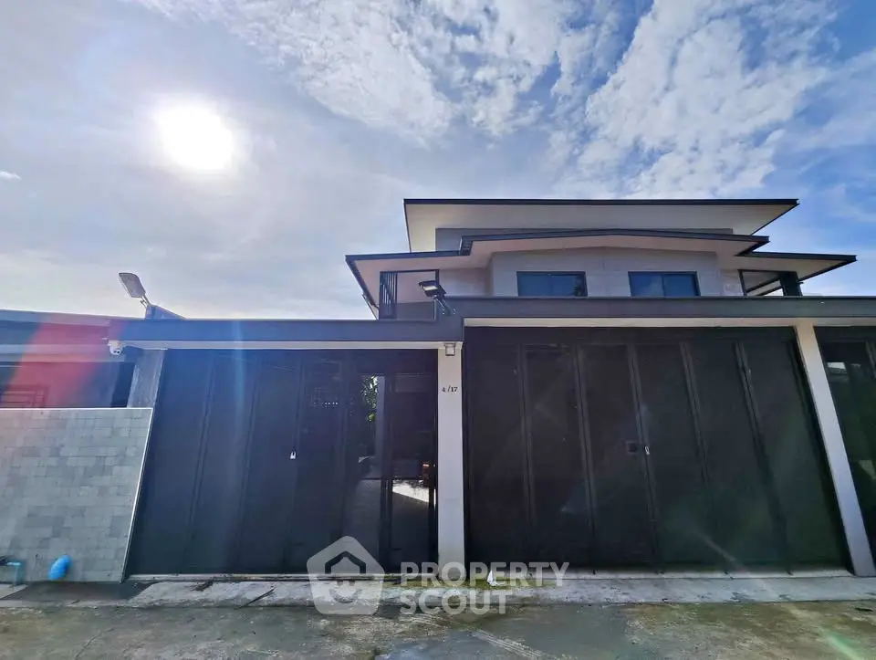Modern two-story house with sleek design and large windows under a bright blue sky.