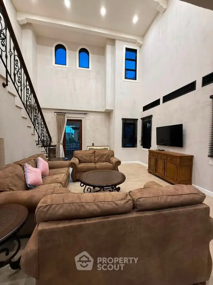 Luxurious high-ceiling living room with elegant staircase and plush seating, perfect for entertaining.