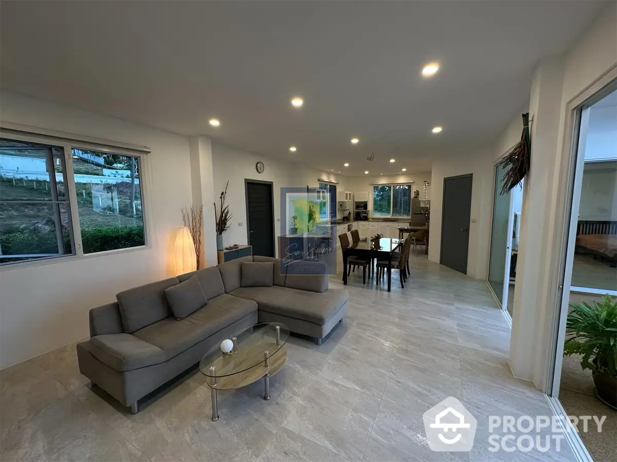 Spacious living room with modern grey sectional sofa, elegant marble flooring, and open layout leading to a well-lit dining area, perfect for entertaining.