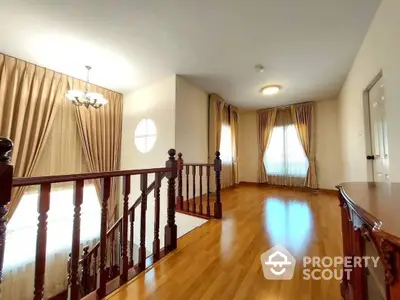 Elegant spacious living area with polished hardwood floors, classic wooden balustrade, and ample natural light from large windows draped in luxurious curtains.