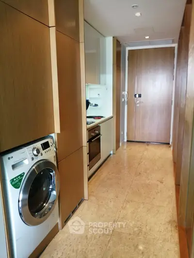 Modern kitchen with sleek wooden cabinetry and built-in appliances, featuring a washing machine and oven.