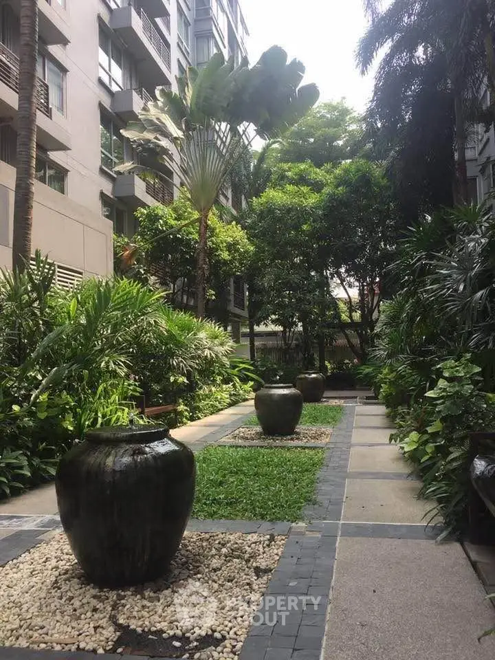 Lush garden courtyard in modern residential complex with elegant planters and tropical greenery.