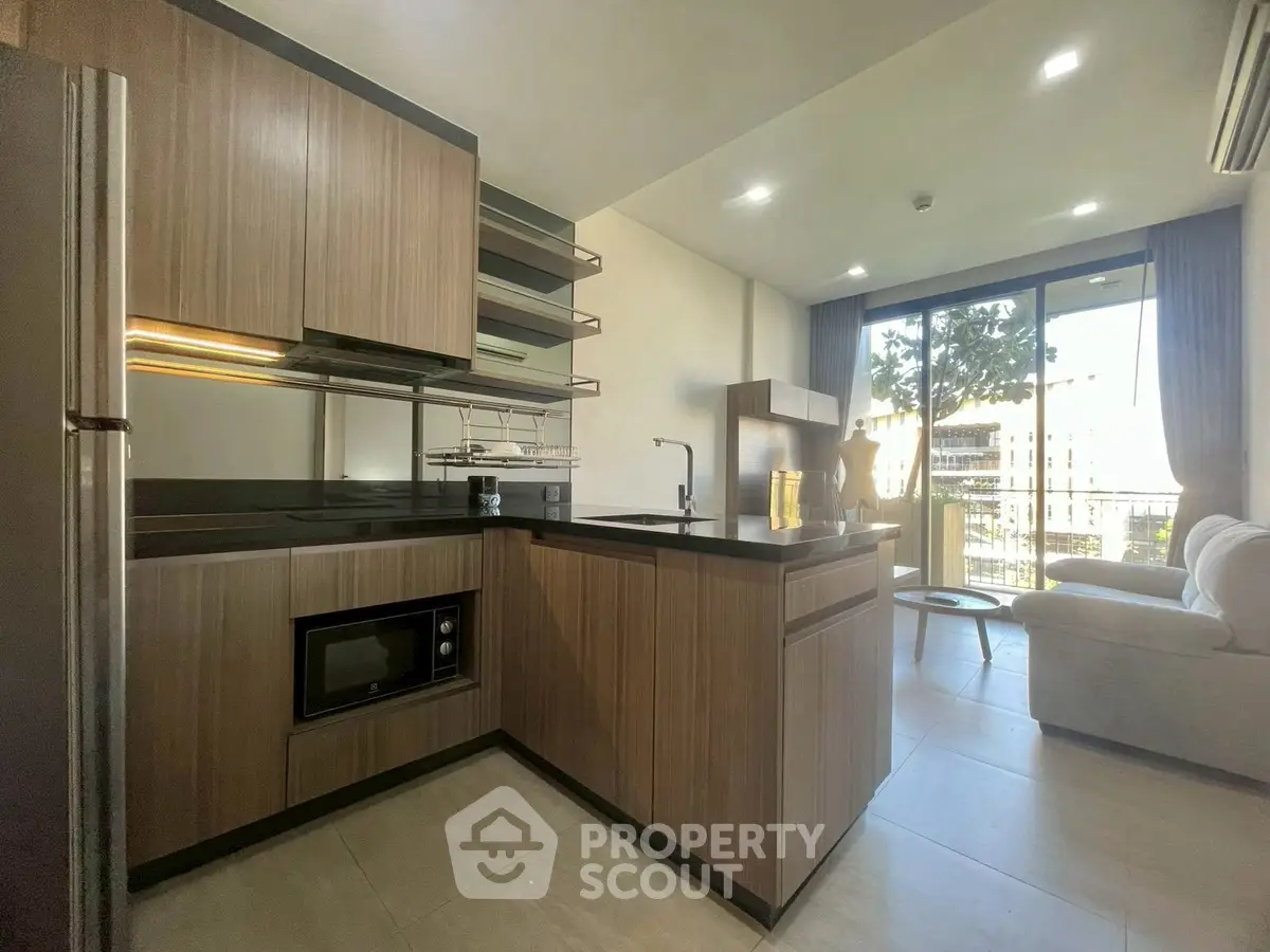 Modern open-layout kitchen with sleek cabinetry and cozy living area, featuring large windows for natural light.