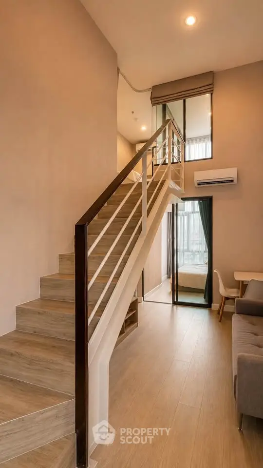 Modern duplex apartment with stylish staircase and cozy living area, featuring large windows for natural light.