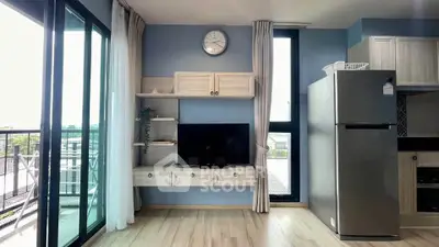Modern living room with balcony view, featuring sleek TV setup and stainless steel fridge.