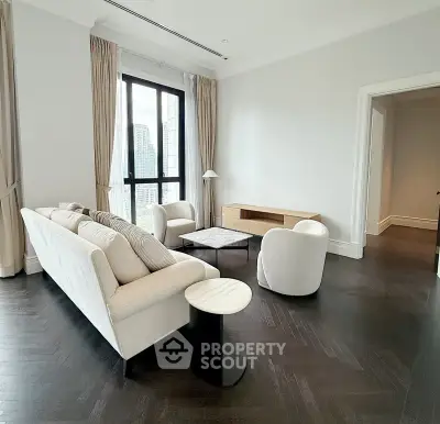 Elegant living room with modern furniture and city view, featuring dark wood flooring and large windows.