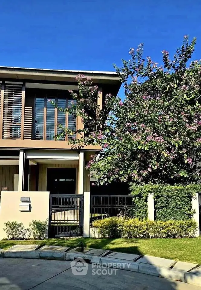 Modern two-story house with lush garden and vibrant flowering tree, perfect for family living.