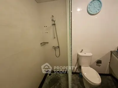 Modern bathroom with shower and toilet, featuring sleek tiles and a wall clock for a contemporary touch.